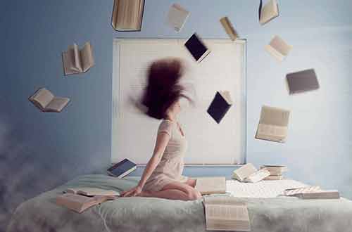 Happy Girl in bed throwing books in the air